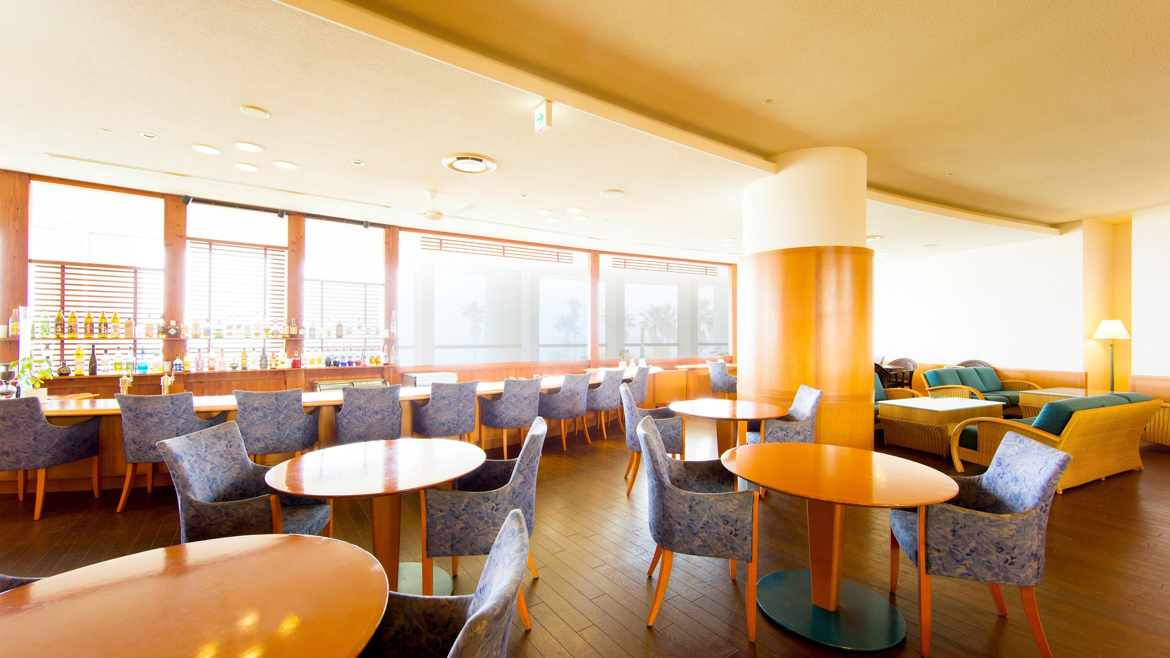 A hotel lobby with round tables, chairs, a bar area, and a seating area with sofas.