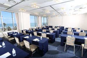 A conference room with tables and chairs, large windows with a view of the ocean, and ceiling lights. - ANA Holiday Inn Resort Miyazaki (Miyazaki)