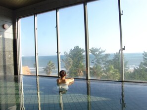 A person in a glass-enclosed infinity pool with a view of the ocean and palm trees. - ANA Holiday Inn Resort Miyazaki (Miyazaki)