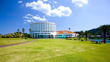A hotel with a circular building, a covered outdoor area with tables and umbrellas, and a grassy lawn.