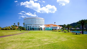 Un hotel con un edificio circular, un espacio al aire libre cubierto con mesas y sombrillas, y un césped.
