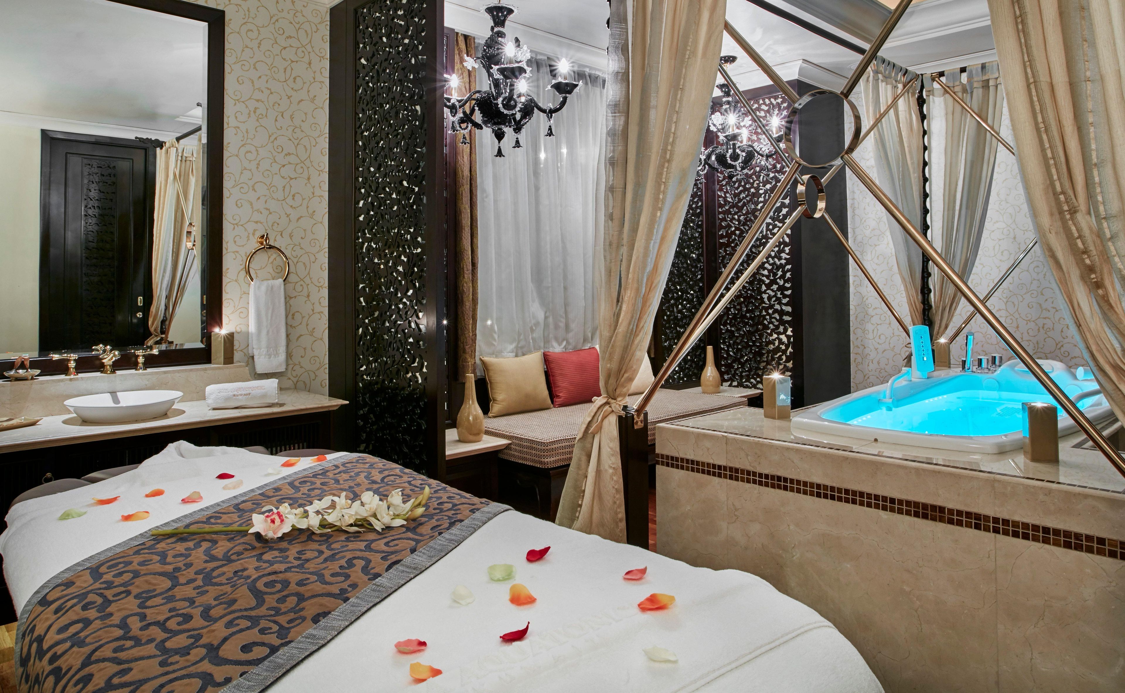 A luxurious bedroom with a large bed, a separate sitting area, a bathtub, and a mirror.