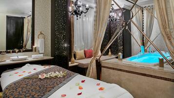 A luxurious bedroom with a large bed, a separate sitting area, a bathtub, and a mirror.