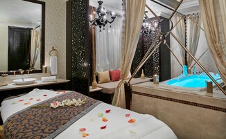 A luxurious bedroom with a large bed, a separate sitting area, a bathtub, and a mirror.