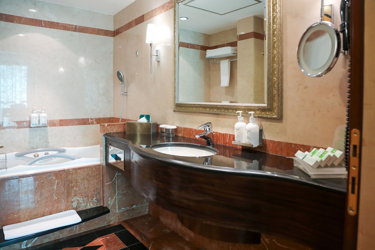 A bathroom with a bathtub, two sinks, a large mirror, and toiletries.