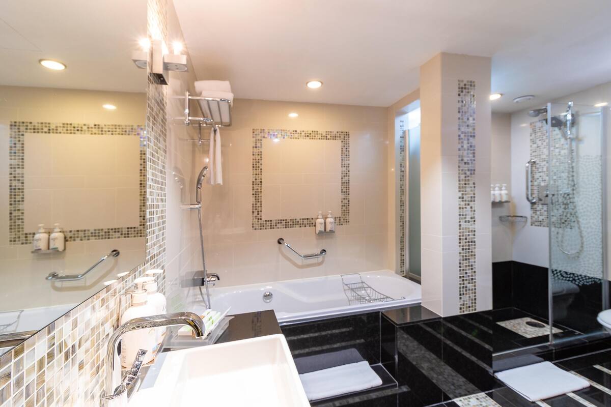 A modern bathroom with a large mirror, a bathtub, a shower area, and a glass-enclosed toilet.