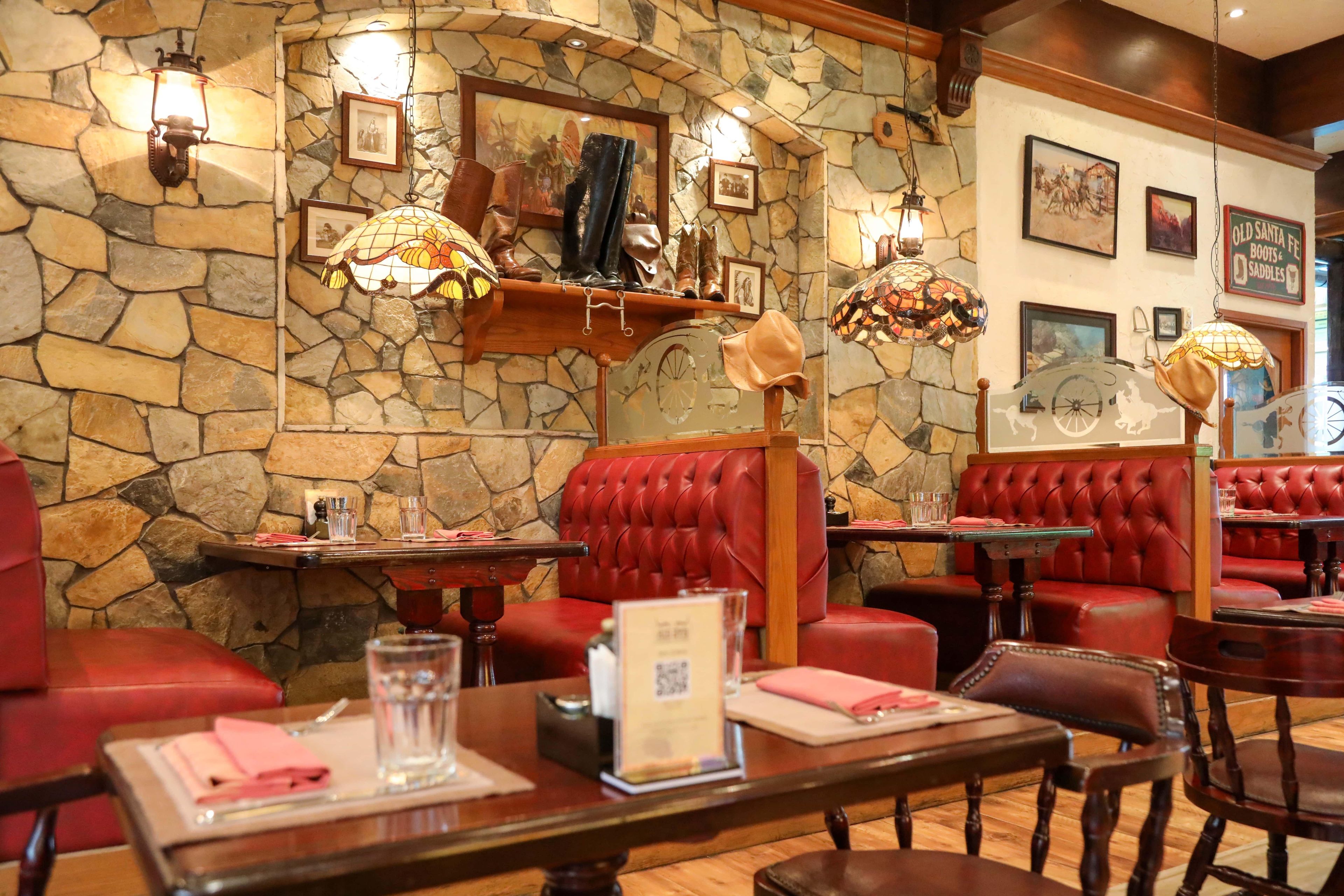 A restaurant interior with stone walls, red leather booths, and hanging lamps.