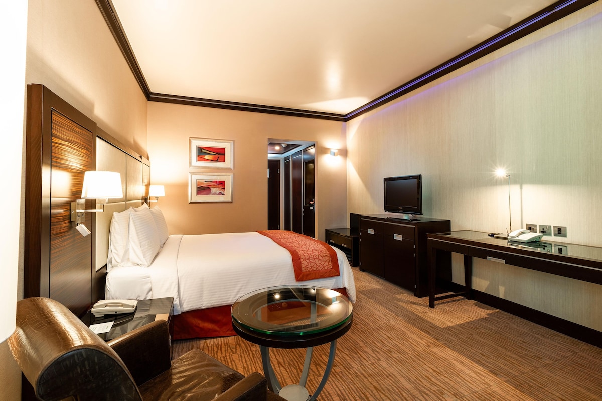A hotel room with a bed, bedside table, lamp, TV, desk, and a mirror.