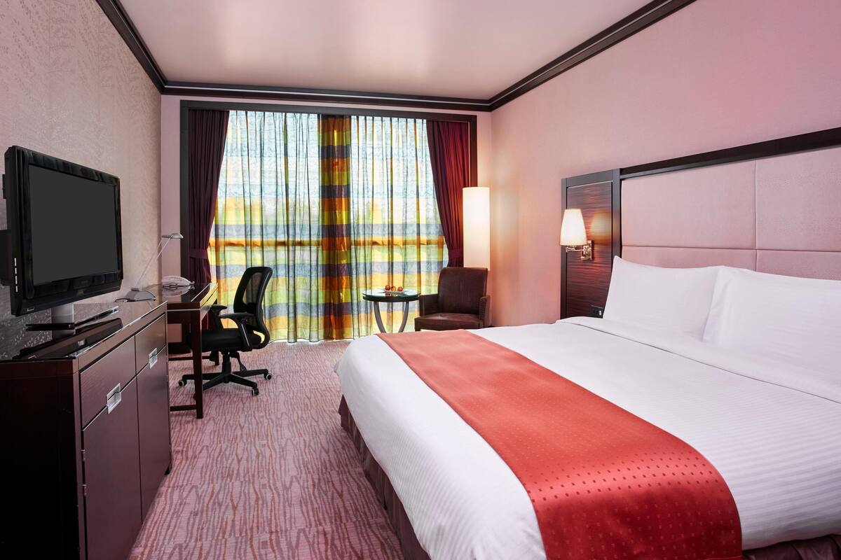 A hotel room with a bed, desk, chair, TV, and curtains.