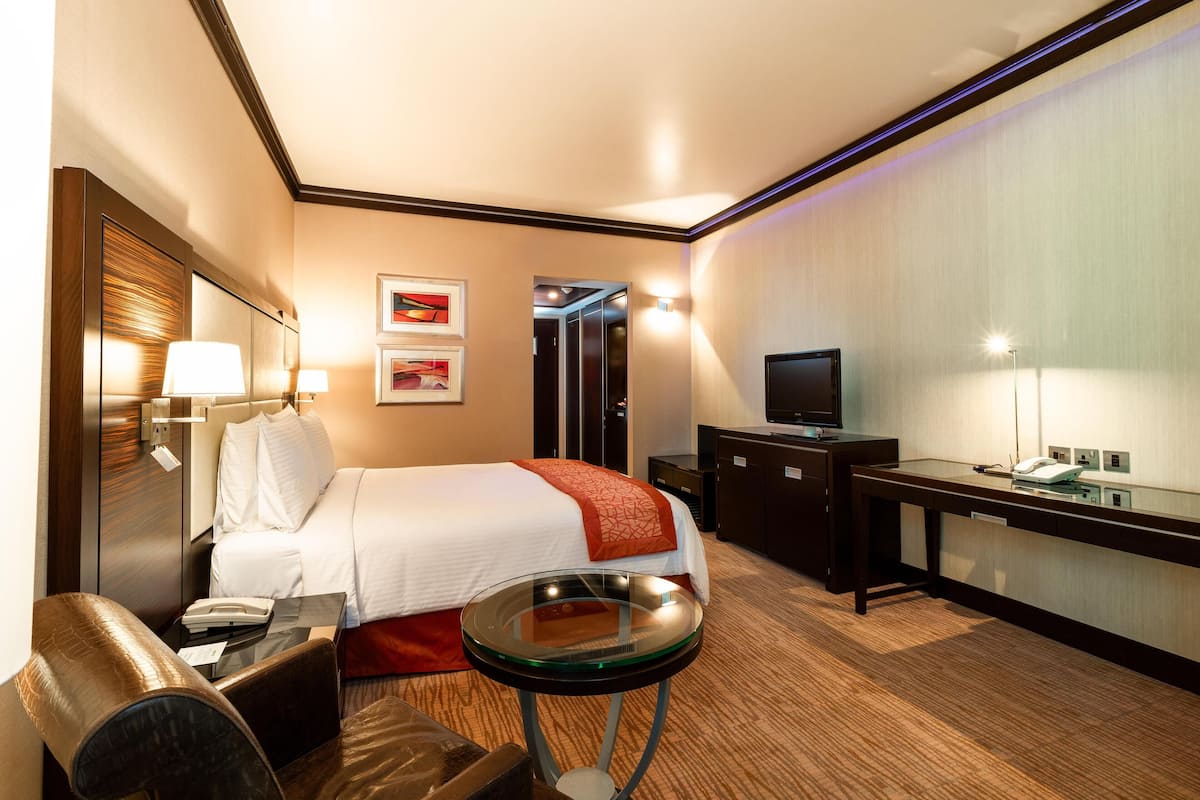 A hotel room with a bed, bedside table, lamp, TV, desk, and a mirror.