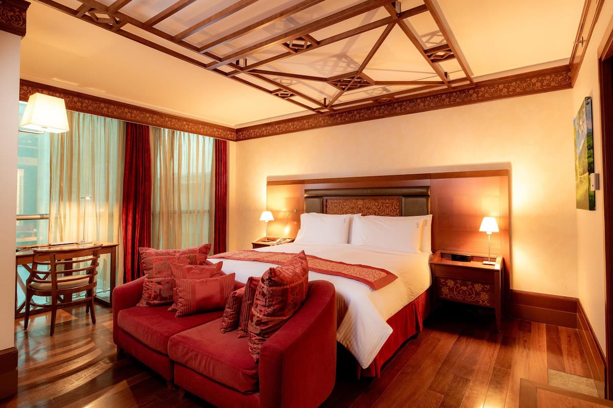 A hotel room with a bed, a red sofa, a wooden desk, and a nightstand with lamps.