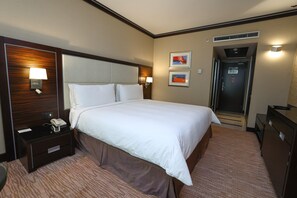 Une chambre d’hôtel avec un grand lit, des lampes de chevet, une table de chevet, un bureau et une porte donnant sur un couloir.