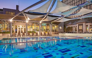 Una piscina con estructura de sombrilla, sillas de descanso y vistas a un edificio con amplios ventanales.