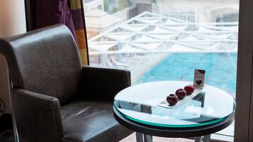 Un sillón de cuero y una mesa de vidrio con una bandeja de fruta en una habitación con vista a una piscina y sombrillas.