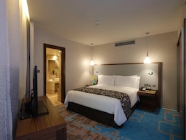 A hotel room with a bed, bedside tables, a desk, a television, and a bathroom visible through an open door.