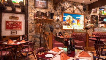 Interior de restaurante con paredes de piedra, muebles de madera y decoración con temática vaquera.