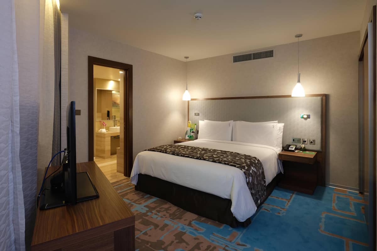 A hotel room with a bed, bedside tables, a desk, a television, and a bathroom visible through an open door.