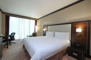 Une chambre d’hôtel avec un grand lit, un bureau avec une chaise, une petite table et une table de chevet avec une lampe.