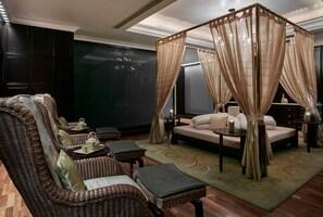 A room with a four-poster bed, a wicker sofa, a small table with a tray, and a green patterned rug. - Holiday Inn Kuwait Al Thuraya City (Farwaniya)