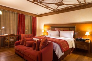 Una habitación de hotel con una cama grande, un sofá, un escritorio con una lámpara y una mesita de noche con lámpara.