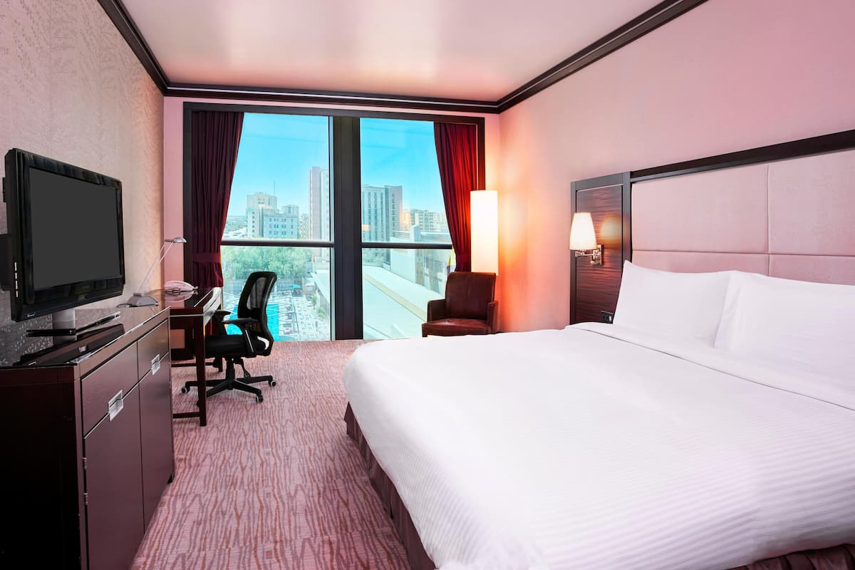A hotel room with a bed, desk, chair, television, and a view of the cityscape.