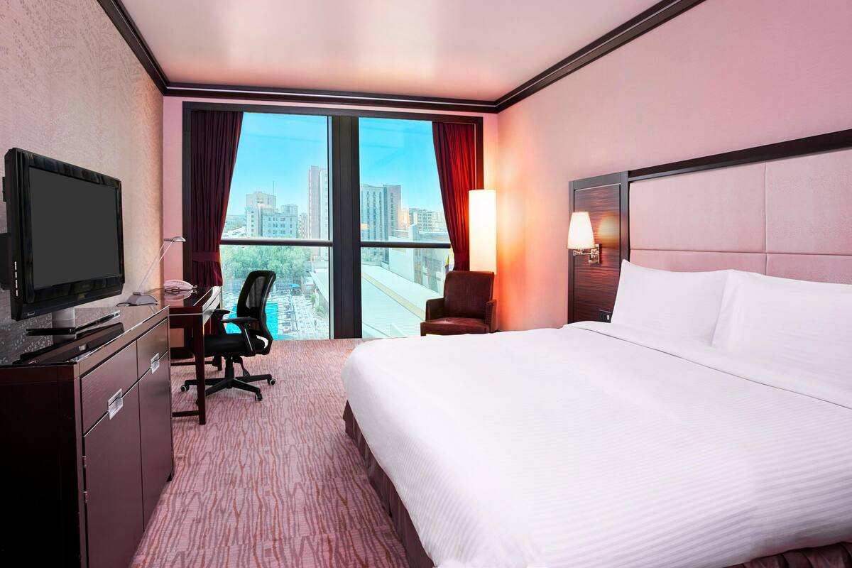 A hotel room with a bed, desk, chair, television, and a view of the cityscape.