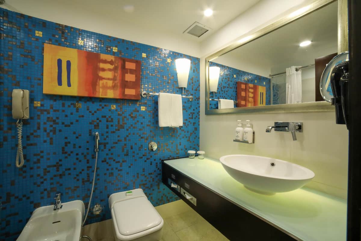 A bathroom with a blue mosaic wall, a white sink, a bidet, a toilet, a mirror, and a hand dryer.