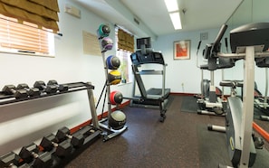 A gym with dumbbells, a treadmill, and weight plates.