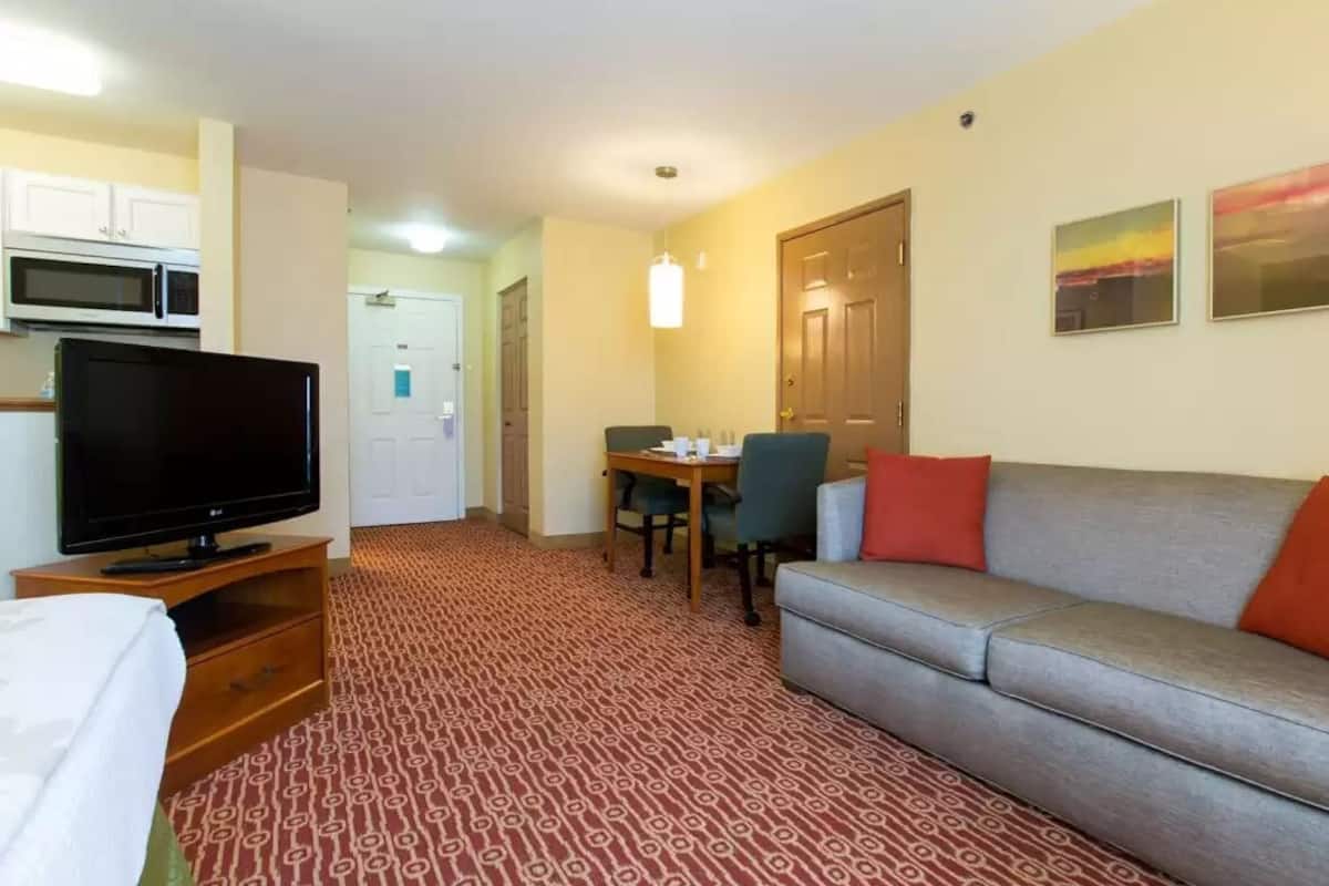 Une chambre d’hôtel équipée d’une télévision, d’un canapé, d’une table à manger avec des chaises, d’un four à micro-ondes et d’un tapis à motifs.