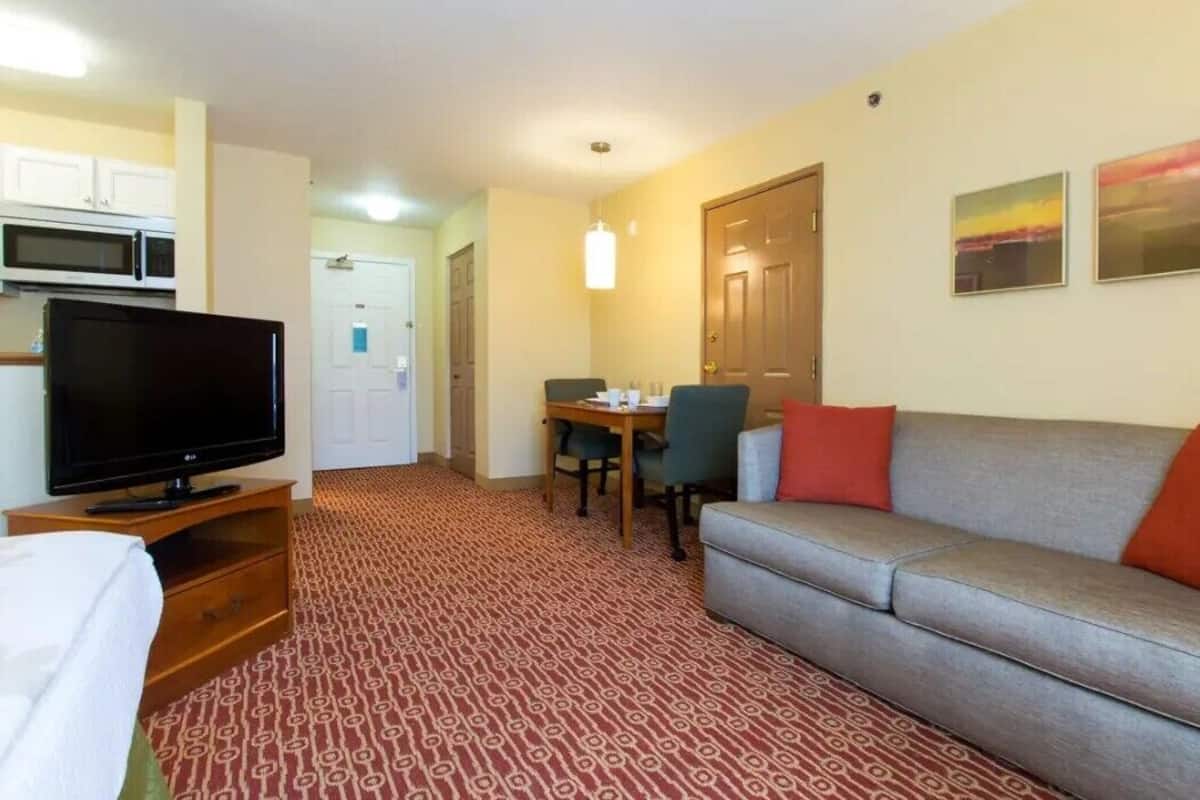 Une chambre d’hôtel équipée d’une télévision, d’un canapé, d’une table à manger, de chaises et d’un tapis à motifs.