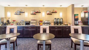 A hotel breakfast area with a buffet, seating, and kitchen appliances. - Dulles Suites (Sterling)