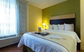 A hotel room with a bed, a bedside table, a lamp, and a window with curtains.
