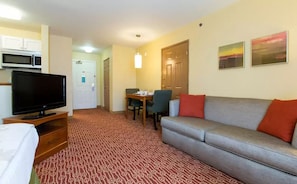 A hotel room with a television, a sofa, a dining table with chairs, a microwave, and a patterned carpet.