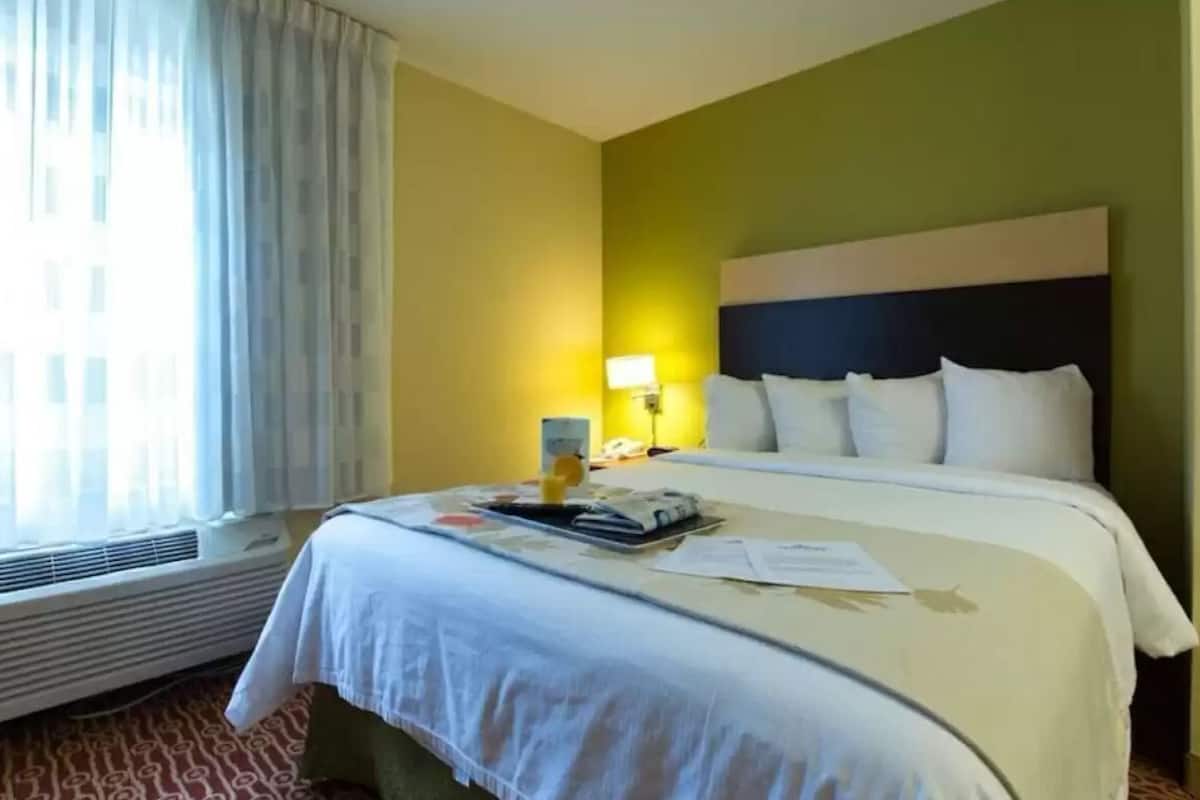 Une chambre d’hôtel avec un lit, une table de chevet, une lampe et une fenêtre avec des rideaux.