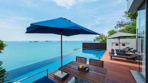 An infinity pool with a view of the sea, a wooden deck with a table and chairs, and a lounge area with umbrellas. - Conrad Koh Samui Resid (Koh Samui)