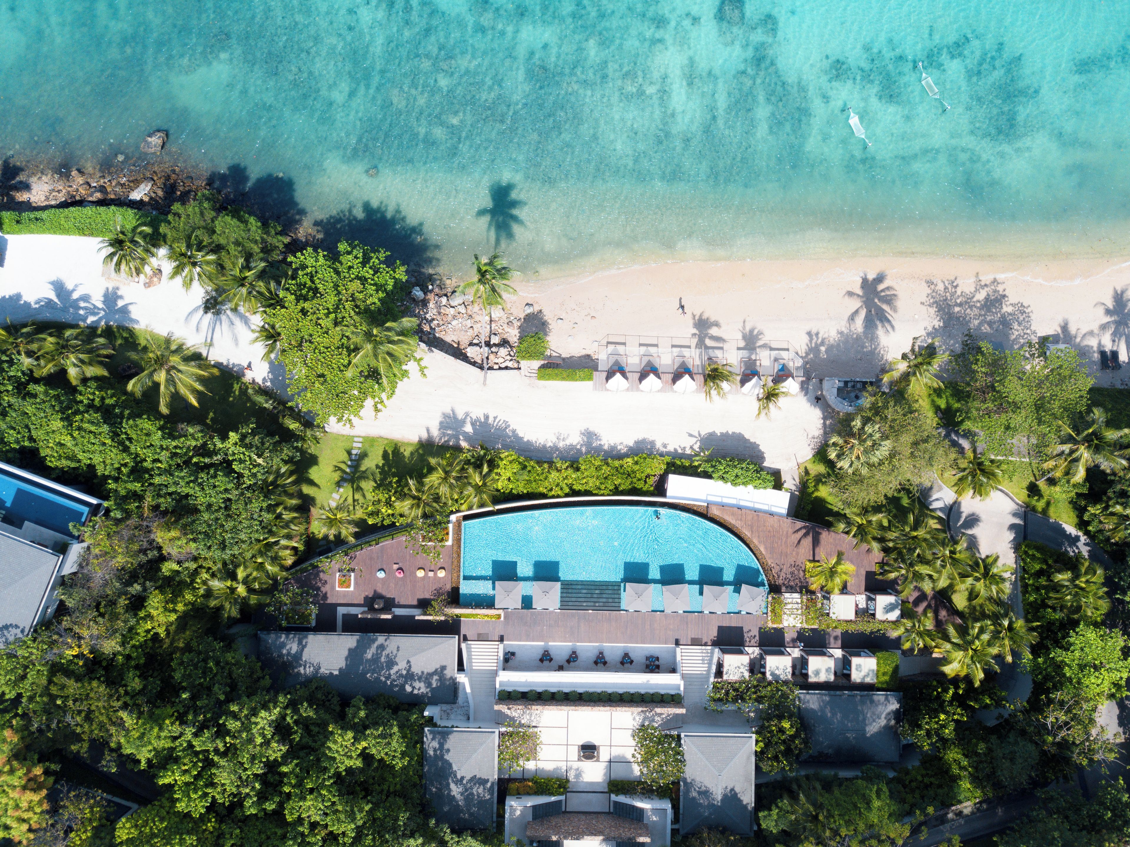 Eine Vogelperspektive eines Resorts mit Schwimmbad, Strand und Palmen.