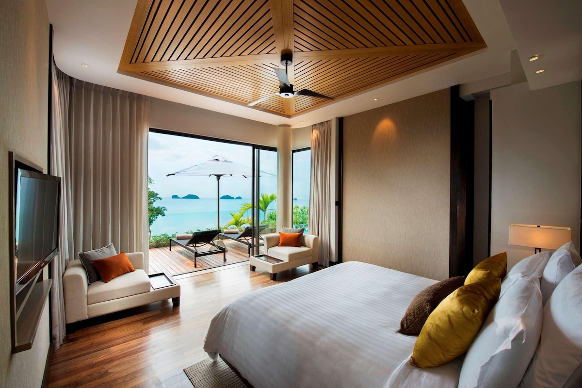 A modern hotel room with a large bed, a flat-screen TV, a sofa, and a dining table.