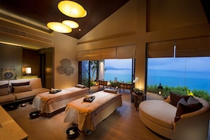 A spa room with two massage tables, a sofa, and a view of the ocean. - Conrad Koh Samui Resid (Koh Samui)