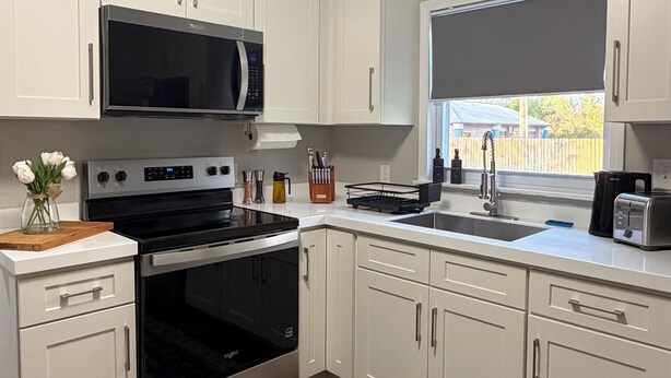 A kitchen with white cabinets, a stainless steel oven, a microwave, and a window with a view of a fence.