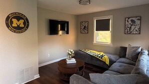 A living room with a couch, a coffee table, a flat-screen TV, and a window with blinds.