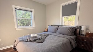 A bedroom with a bed, wooden flooring, a nightstand, a lamp, and a window.