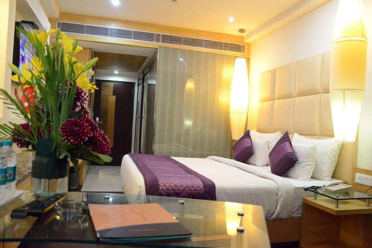 A hotel room with a bed, bedside table, lamp, and a vase with flowers.