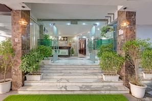 A hotel lobby with marble flooring, glass doors, and potted plants.