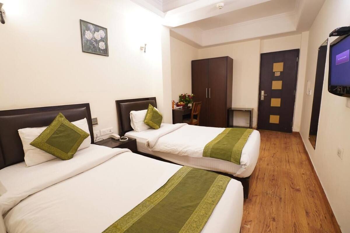 A hotel room with two beds, a desk, a wardrobe, and a television.