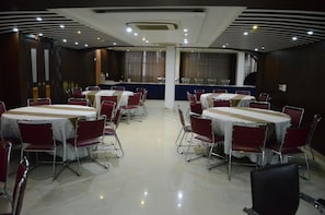 Un salón de conferencias con varias mesas y sillas, un mostrador central y un diseño de techo moderno.