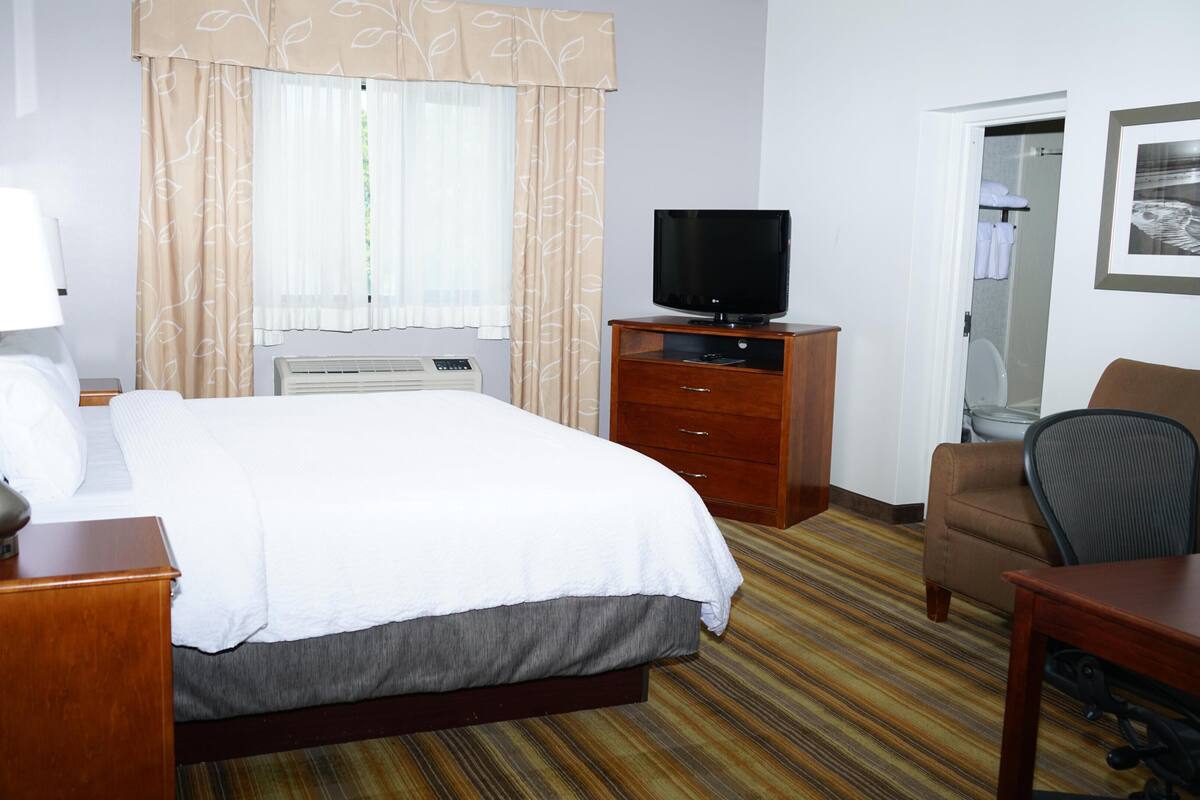 A hotel room with a bed, a desk, a chair, a television, and a window with curtains.
