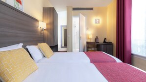A hotel room with two beds, a desk, a chair, a window with curtains, and a door leading to another room.