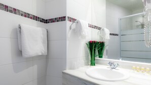 A modern bathroom with white tiles, a marble sink, and a glass shower enclosure.