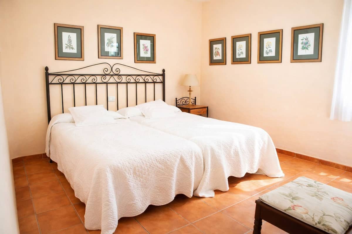 Una cama doble con ropa blanca, una mesita de noche con lámpara e impresiones botánicas enmarcadas en la pared.