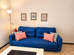 A blue sofa with two pink and one striped pillow, a white coffee table, and three framed artworks on the wall. - One bedroom, balcony, Wi-Fi, El Médano centre (El Médano)